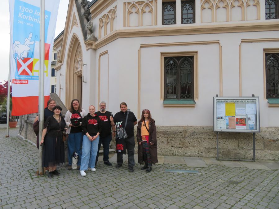 Vor der Kirche in Rosenheim stehen die Kohlrabenschwarz Fans. Drei im Cosplay: Perchta, Pfarrer Franz und Susanne.