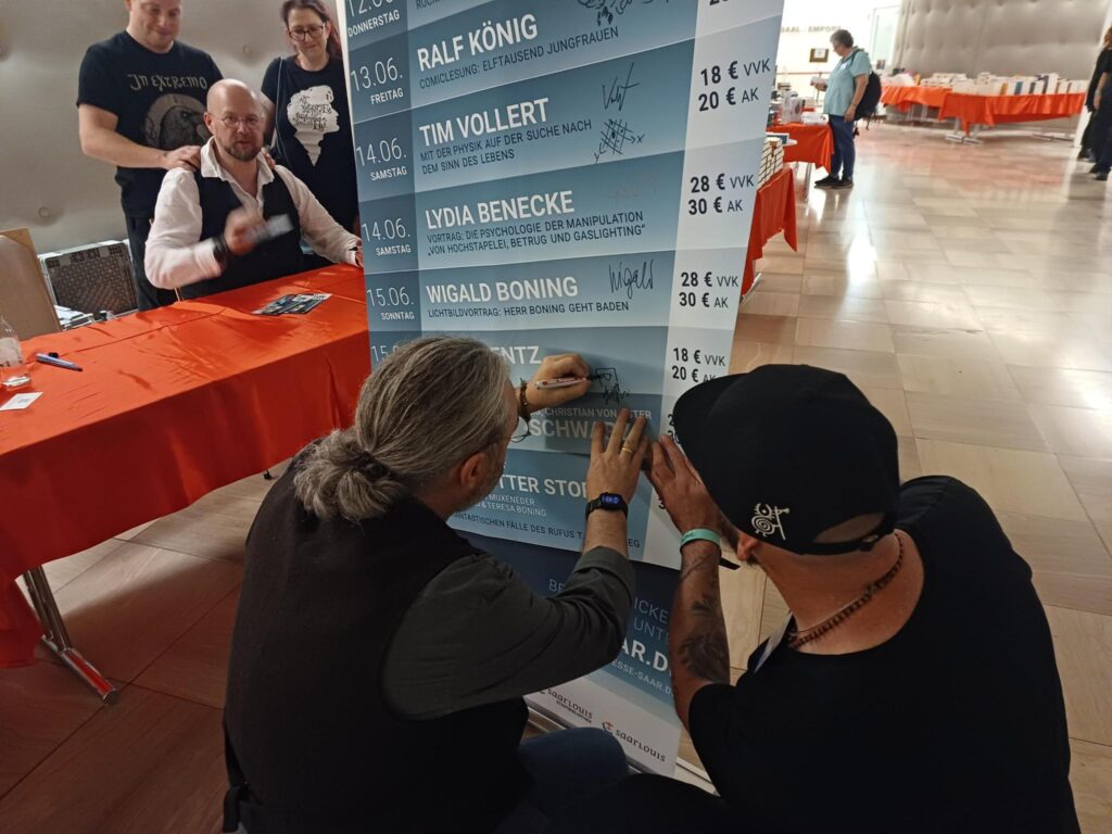 Tommy Krappweis unterschreibt auf dem Aufsteller mit dem Programm der Buchmesse Saar.
